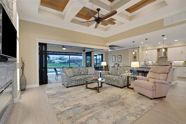 living room with a high ceiling, coffered ceiling, visible vents, ornamental molding, and light wood finished floors