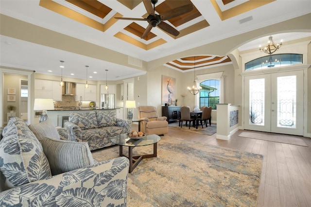 living area with arched walkways, light wood-style flooring, coffered ceiling, french doors, and ornamental molding