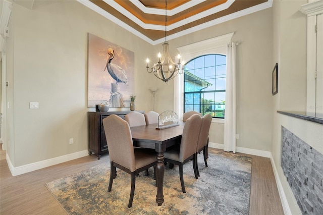 dining area featuring ornamental molding, a tray ceiling, a notable chandelier, and light wood-style flooring