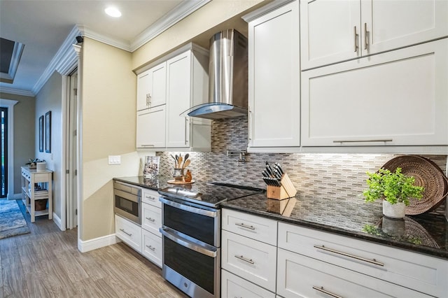 kitchen with white cabinets, dark stone counters, wall chimney exhaust hood, stainless steel appliances, and backsplash