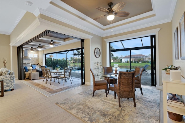 dining area featuring a sunroom, wood finished floors, a raised ceiling, and a wealth of natural light