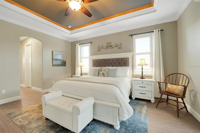 bedroom featuring arched walkways, a tray ceiling, multiple windows, and baseboards