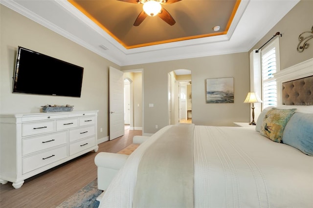 bedroom with light wood-style flooring, arched walkways, a raised ceiling, and baseboards