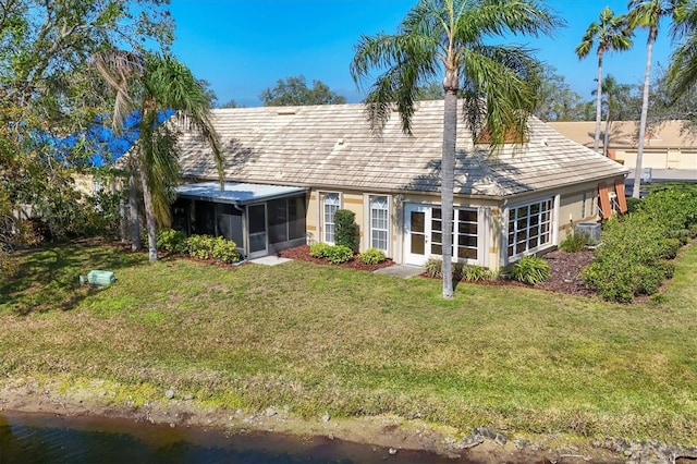 back of house featuring a water view, a sunroom, and a lawn