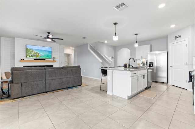 kitchen featuring pendant lighting, sink, stainless steel appliances, white cabinets, and a center island with sink