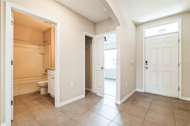 foyer with baseboards, arched walkways, ceiling fan, a textured ceiling, and light tile patterned flooring