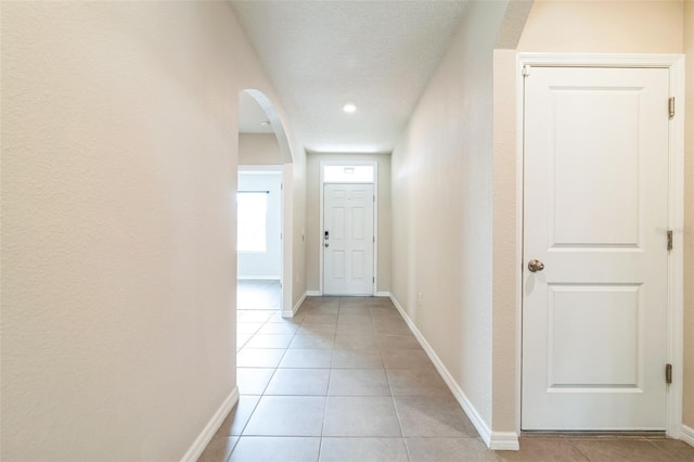 doorway to outside with light tile patterned floors, a textured ceiling, arched walkways, and baseboards