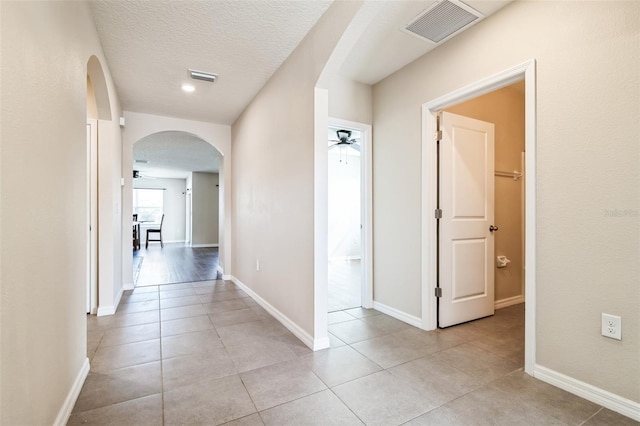 hallway featuring visible vents, arched walkways, a textured ceiling, and light tile patterned flooring