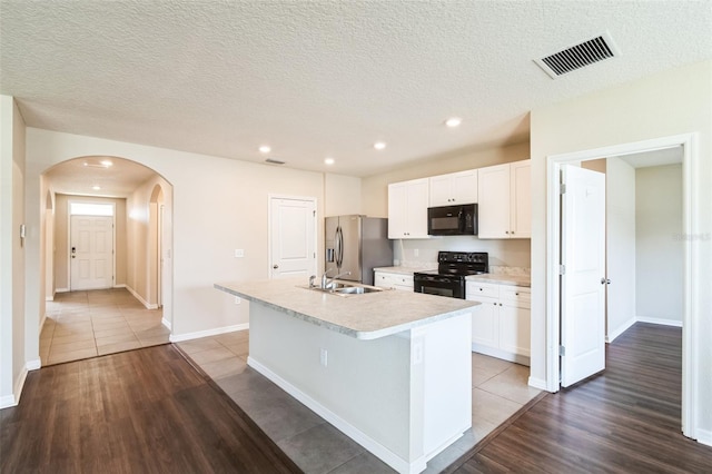 kitchen featuring visible vents, an island with sink, light countertops, black appliances, and white cabinetry