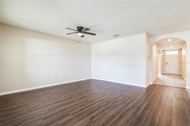 unfurnished room featuring visible vents, a textured ceiling, arched walkways, and dark wood-style flooring