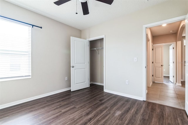 unfurnished bedroom featuring a textured ceiling, a ceiling fan, baseboards, a closet, and dark wood finished floors