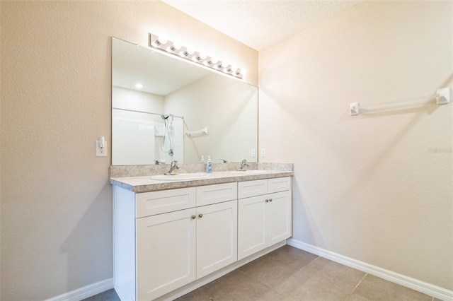 full bath featuring double vanity, a sink, tile patterned flooring, baseboards, and walk in shower