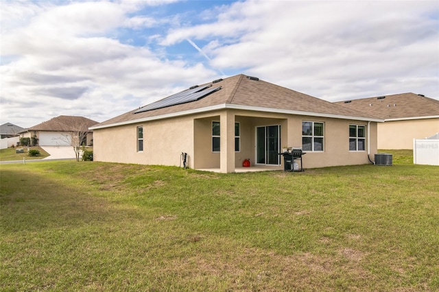 rear view of house with a yard, central AC unit, solar panels, and stucco siding