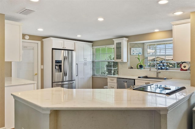 kitchen with white cabinetry, light stone counters, stainless steel appliances, and kitchen peninsula