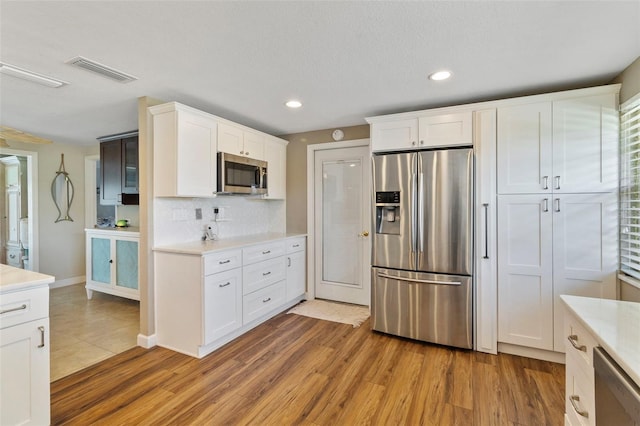 kitchen featuring tasteful backsplash, hardwood / wood-style flooring, white cabinets, and appliances with stainless steel finishes