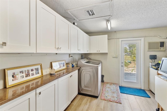 laundry room with light hardwood / wood-style flooring, a wall unit AC, cabinets, a textured ceiling, and washer / dryer