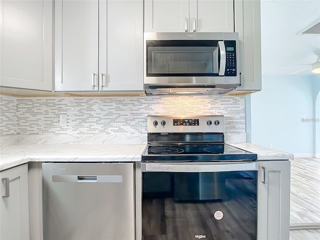 kitchen with stainless steel appliances, tasteful backsplash, light stone counters, and light hardwood / wood-style floors