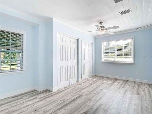 unfurnished bedroom with crown molding, ceiling fan, light hardwood / wood-style floors, and two closets