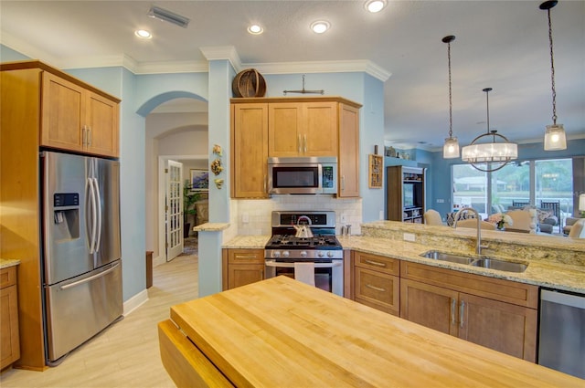 kitchen featuring appliances with stainless steel finishes, butcher block countertops, decorative light fixtures, sink, and decorative backsplash