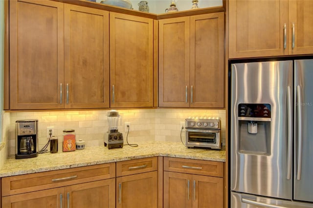 kitchen with light stone counters, stainless steel fridge, and tasteful backsplash