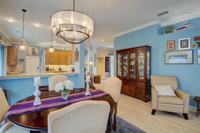 dining area featuring an inviting chandelier, crown molding, sink, and light hardwood / wood-style flooring