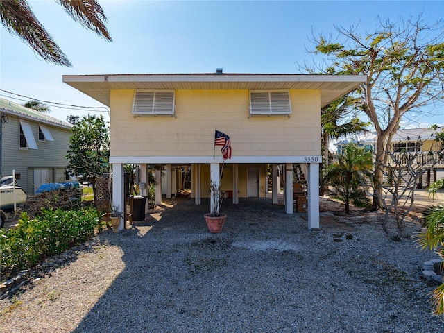 rear view of property with dirt driveway, a carport, and stairway