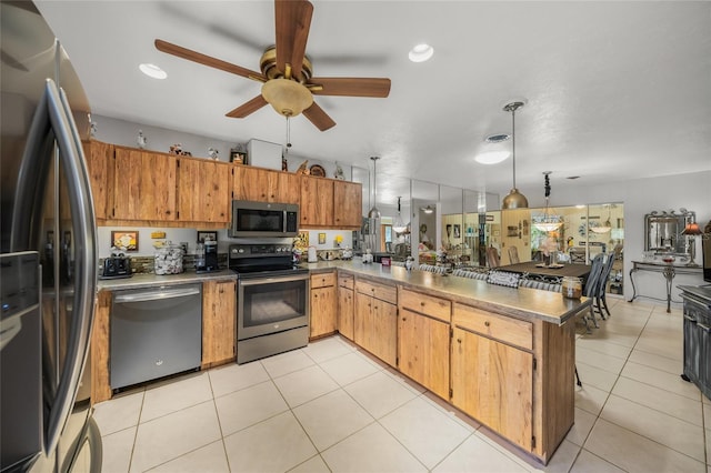 kitchen featuring brown cabinets, a peninsula, stainless steel appliances, pendant lighting, and light tile patterned flooring