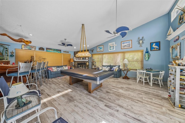 recreation room featuring baseboards, ceiling fan, wood finished floors, a fireplace, and high vaulted ceiling