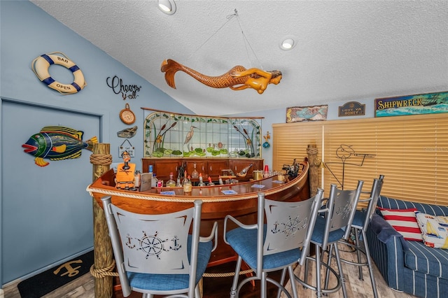 bar with lofted ceiling, a bar, and a textured ceiling