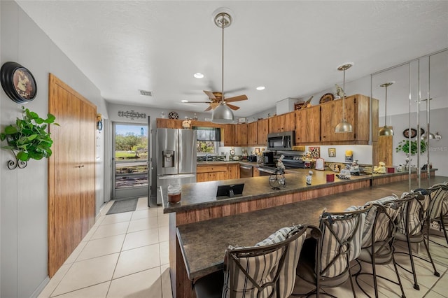 kitchen with dark countertops, a peninsula, appliances with stainless steel finishes, and a kitchen breakfast bar