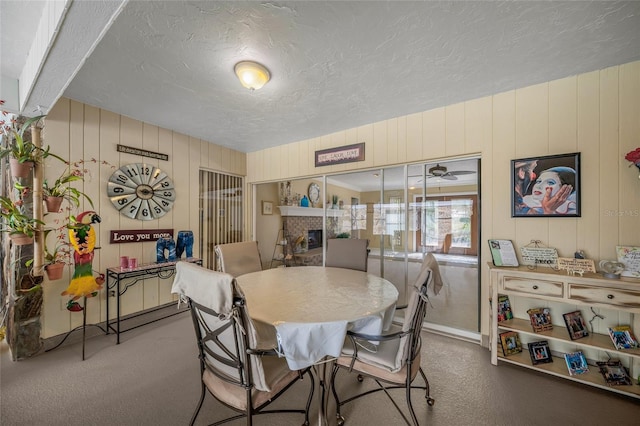 carpeted dining area with a brick fireplace, a ceiling fan, and a textured ceiling