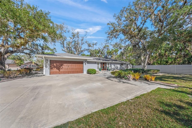 single story home featuring an attached garage, fence, concrete driveway, stucco siding, and a front yard