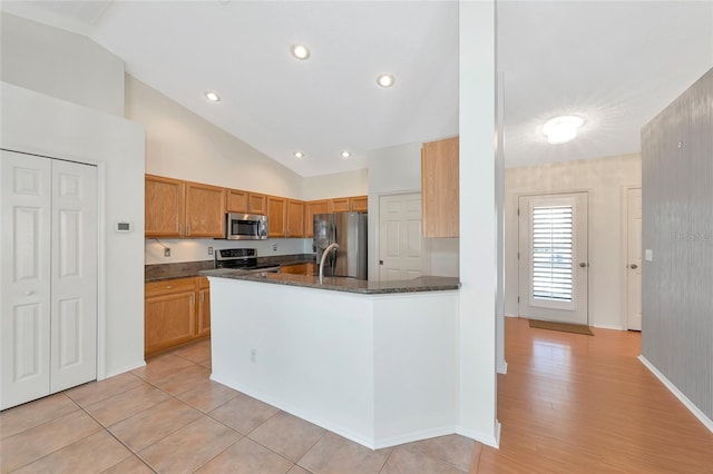 kitchen with stainless steel appliances, lofted ceiling, kitchen peninsula, and dark stone counters