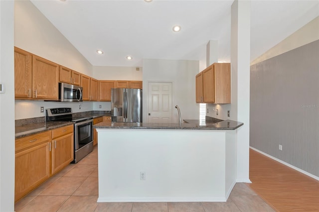 kitchen featuring vaulted ceiling, light tile patterned floors, dark stone counters, kitchen peninsula, and stainless steel appliances