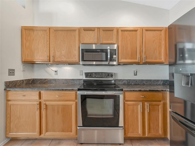 kitchen with dark stone countertops, stainless steel appliances, and light tile patterned flooring