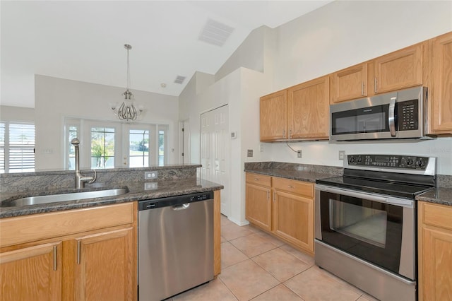 kitchen featuring sink, light tile patterned floors, appliances with stainless steel finishes, dark stone countertops, and decorative light fixtures