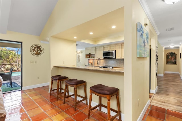 kitchen with tasteful backsplash, ornamental molding, light stone countertops, and a kitchen bar