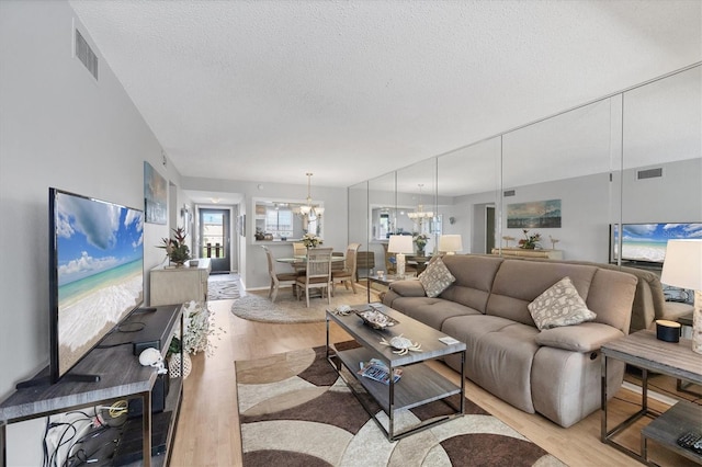 living room with a textured ceiling, an inviting chandelier, and light hardwood / wood-style floors