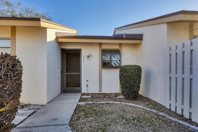 view of exterior entry featuring fence and stucco siding