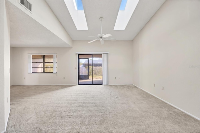 empty room with carpet floors, visible vents, ceiling fan, vaulted ceiling with skylight, and baseboards