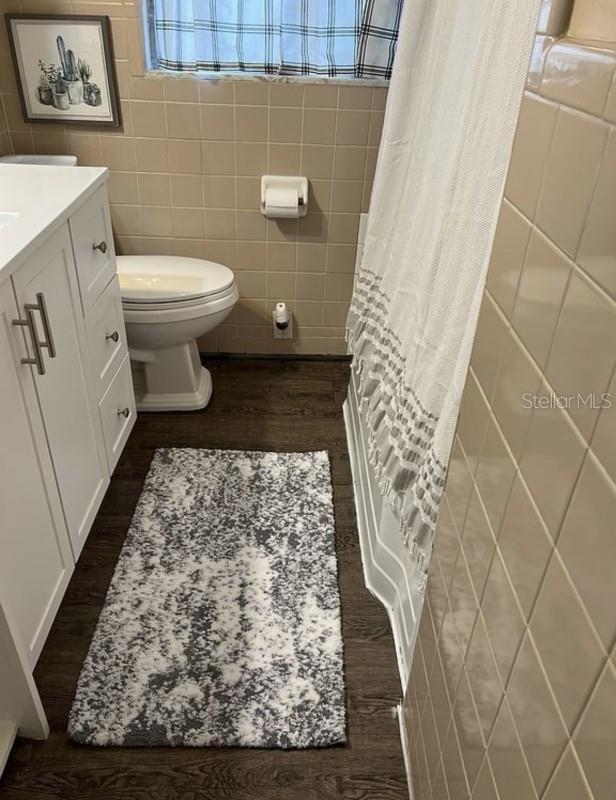 bathroom featuring vanity, wood-type flooring, tile walls, and toilet