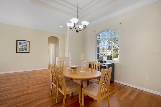 dining area with hardwood / wood-style floors, crown molding, a raised ceiling, and a chandelier