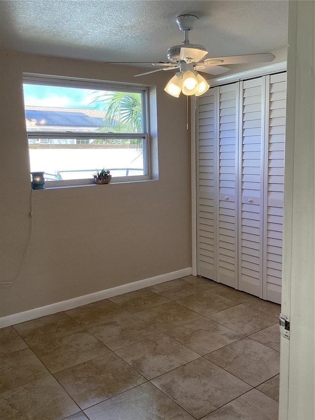 unfurnished bedroom featuring a textured ceiling, a closet, light tile patterned flooring, and ceiling fan