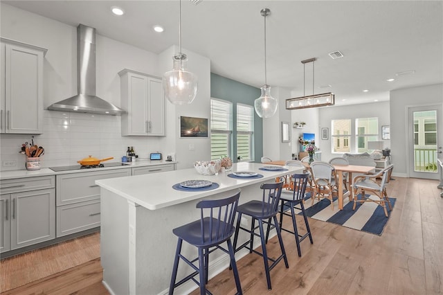 kitchen with tasteful backsplash, wall chimney exhaust hood, black electric cooktop, light countertops, and light wood-style floors