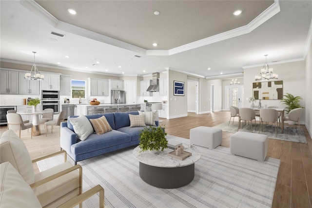 living room with a chandelier, recessed lighting, a raised ceiling, and light wood-style floors