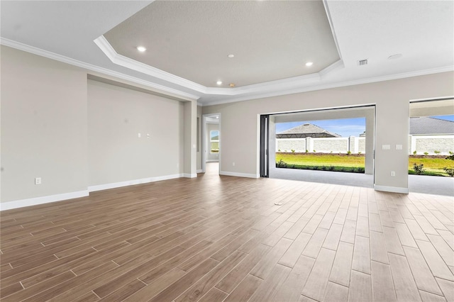 unfurnished living room with ornamental molding, a tray ceiling, and wood finish floors