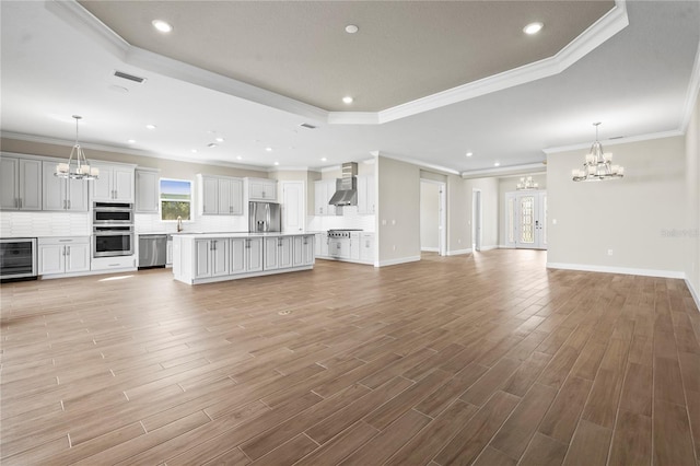 unfurnished living room featuring a notable chandelier, beverage cooler, baseboards, light wood-type flooring, and a tray ceiling