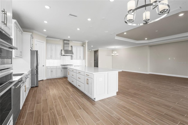 kitchen featuring a chandelier, white cabinets, light countertops, wall chimney range hood, and a center island