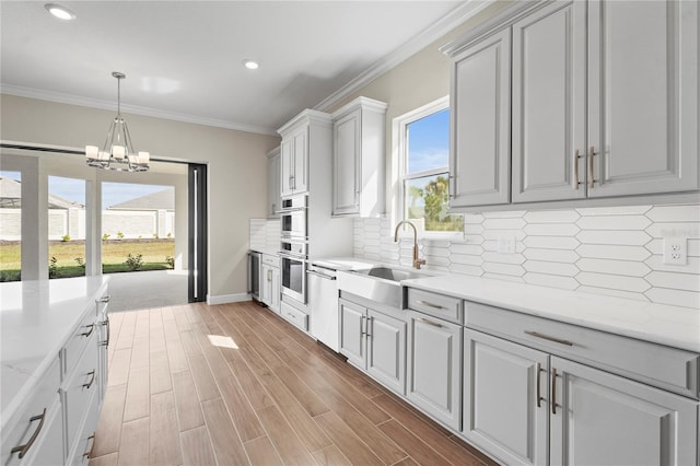 kitchen with light wood-type flooring, plenty of natural light, ornamental molding, and a sink