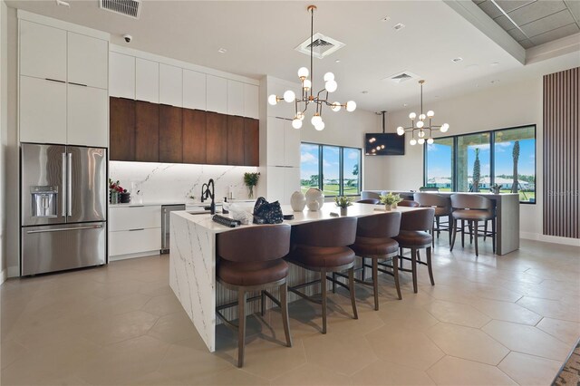 kitchen with modern cabinets, high end refrigerator, pendant lighting, and a center island with sink